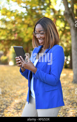 Black businesswoman in blue blazer standing outdoors while using a digital tablet. Stock Photo