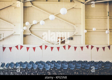 Red White Blue, warehouse celebration. White hanging lanterns, red triangle flag banner, blue chairs lined up. No people, empty auditorium venue Stock Photo