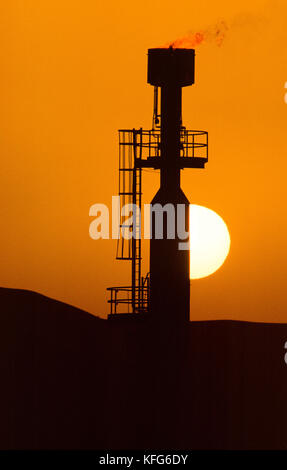 Sun sets behind a gas flare of the  Shaybah Gas Oil Separation Plant (GOSP), a major gas and oil production facility located in the empty quarter desert of Saudi Arabia, near the border of the UAE. Stock Photo