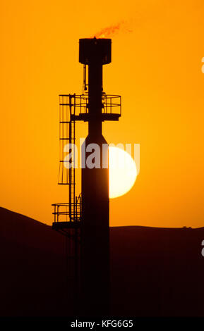 Sun sets behind a gas flare of the  Shaybah Gas Oil Separation Plant (GOSP), a major gas and oil production facility located in the empty quarter desert of Saudi Arabia, near the border of the UAE. Stock Photo