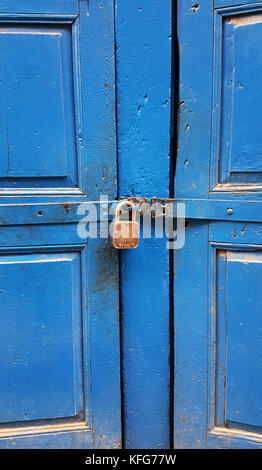 Rusty orange lock covers the wooden blue doors, rectangular frames on the doors. Stock Photo