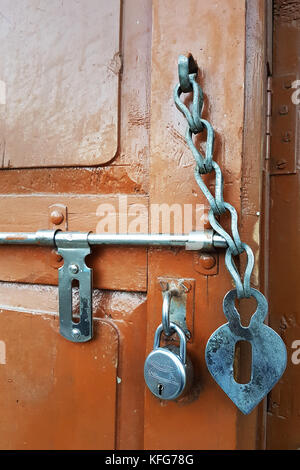 Brown wooden door on which a vintage latch, a metal lock and an old door chain, unusual interior elements. Stock Photo