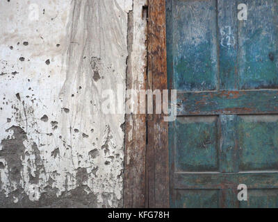White wall of a village house with spots of mud and a vintage green door, worn from a long use, left an empty place for text on the left. Stock Photo