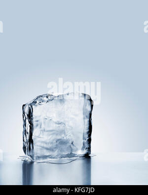 Cold blue crystal clear frozen block of ice melting to create pool of water on scratched steel surface Stock Photo