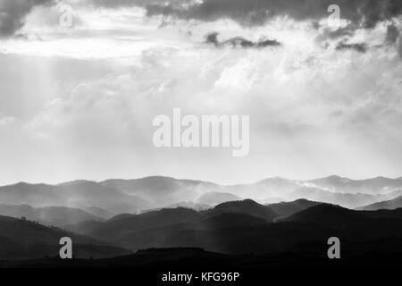 Various layers of hills and mountains with mist between them, with sun rays coming out through the clouds Stock Photo