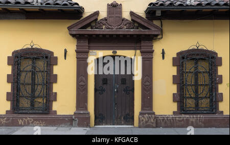 Very old yellow building with brown window and door details and black wrought iron bars on windows.  Wood doors with large black hinges and tile roof. Stock Photo