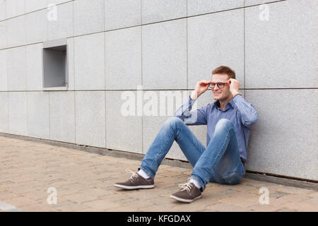 happy man sitting on the ground, leaning against the wall. Stock Photo