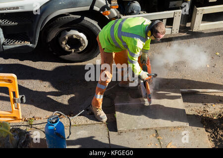 Team of lighting contractors reinstate pavement and cut concrete slabs to size with an angle grinder after fitting street lighting column. London UK Stock Photo