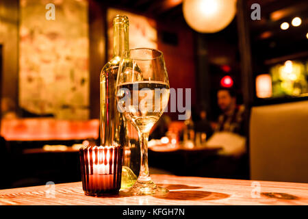 Wine glass, bottle and candle on table in restaurant with warm light Stock Photo