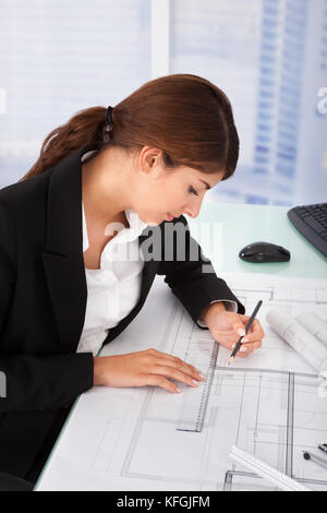 Young female architect working on blueprint at desk in office Stock Photo