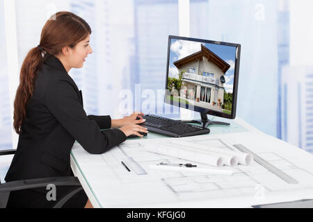 Side view of young female architect surfing house on computer at desk in office Stock Photo