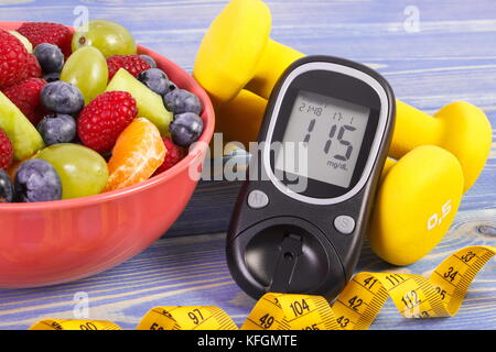 Fresh fruit salad, glucose meter with result of sugar level, tape measure and dumbbells for fitness, concept of diabetes, sport, diet, slimming, healt Stock Photo