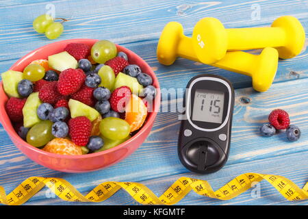 Fresh fruit salad, glucose meter with result of sugar level, tape measure and dumbbells for fitness, concept of diabetes, sport, slimming, healthy lif Stock Photo