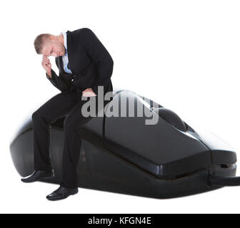 Worried businessman sitting on a computer mouse with his head in his hand in despair  conceptual of online communication and e-commerce Stock Photo