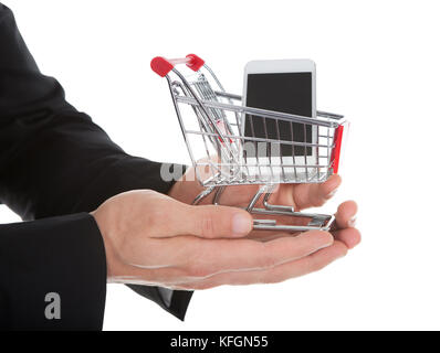Businessman holding a shopping cart and tablet cupped in his hands conceptual of e-commerce and online shopping  isolated on white Stock Photo