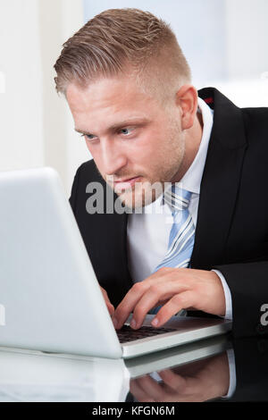 Businessman leaning forward staring intently at his laptop screen as he types information on the keyboard while sitting at his desk  close up portrait Stock Photo