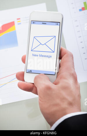 New email message icon on a mobile phone held in the hand of a businessman as he checks his mail at work Stock Photo