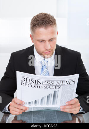 Stylish handsome businessman studying the financial newspaper or Business News while seated at his desk concentrating on the articles Stock Photo