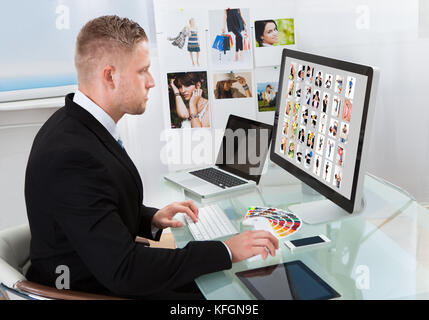 Businessman sitting at his desk in front of a large screen monitor editing photographs Stock Photo