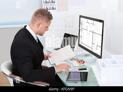 Businessman analyzing a spreadsheet online checking against a document in his hand to collate the information Stock Photo