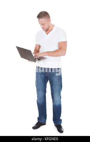 Smiling man in jeans standing using a handheld laptop computer balanced on his palm as he looks at the camera with a friendly smile  isolated on white Stock Photo