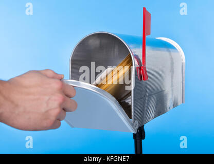 Man opening his mailbox to remove mail inside  close up of his hand on the open door against a blue sky Stock Photo
