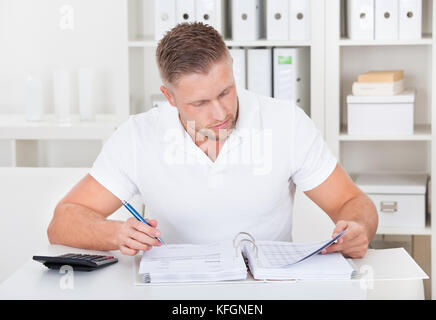 Businessman working at his desk in the office sitting writing notes in a short-sleeved white shirt Stock Photo