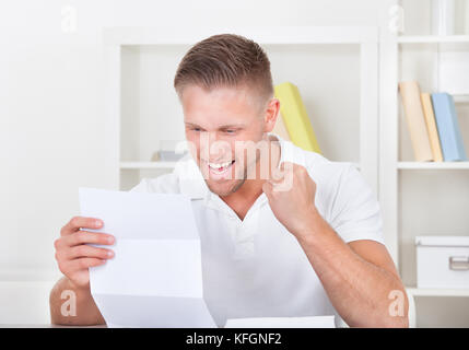 Man cheering in jubilation as he reads a letter punching the air with his fist as he reads the good news Stock Photo