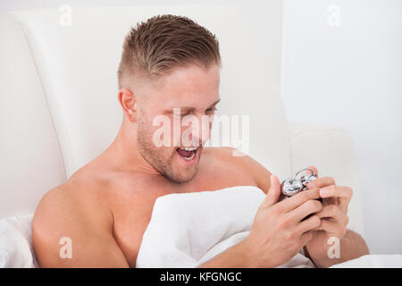 Man screaming in frustration at his alarm clock as it wakes him up after a  sleepless night Stock Photo