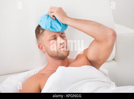 Man nursing a hangover after a heavy night of partying holding an ice pack to his forehead with his eyes closed on pain against the throbbing Stock Photo