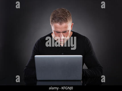 Man or hacker working on a laptop computer at night bending forwards over the keyboard in the glow from the screen as he browses the internet or retri Stock Photo