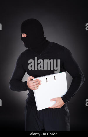 Thief in a balaclava stealing a file with information as he furtively makes his escape in the darkness  conceptual of data and identity theft Stock Photo