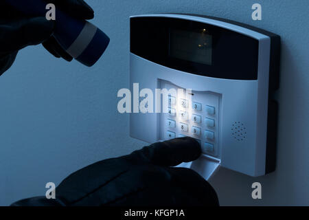 Burglar With Flashlight Trying To Disarm The Security Alarm System Stock Photo