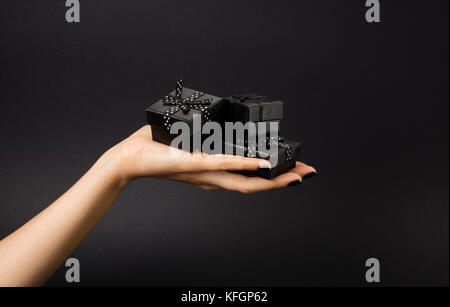 Female hand holding a three black gift boxes on a palm. Isolated on black background. Shallow depth photo. Stock Photo