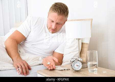 Portrait Of Young Man Lying On Bed Taking Medicines Stock Photo