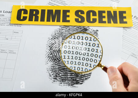 Person Hand With Magnifying Glass Over Document Revealing Binary Code And Crime Scene Tape On It Stock Photo