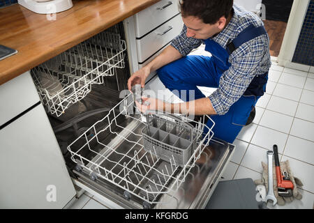 Portrait Of Male Technician Repairing Dishwasher In Kitchen Stock Photo