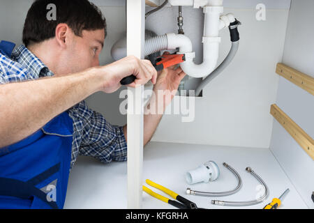 Portrait Of Male Plumber Fixing A Sink In Bathroom Stock Photo