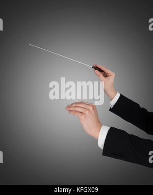 Closeup of music conductor's hands holding baton against gray background Stock Photo