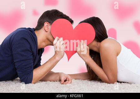Profile shot of couple kissing behind heart while lying on fur Stock Photo