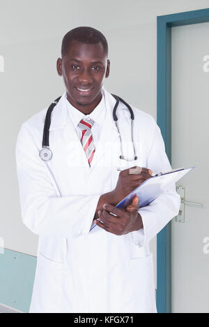Portrait of confident young doctor writing notes on clipboard in hospital Stock Photo