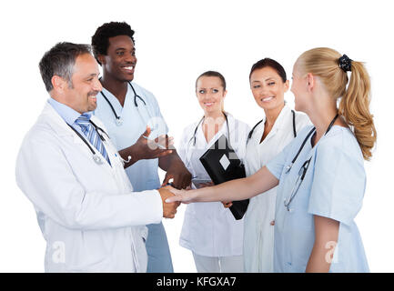 Male and female doctors making handshake while colleagues looking at them over white background Stock Photo