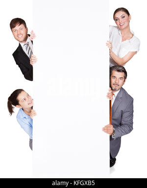 Portrait of happy businesspeople hiding behind large billboard over white background Stock Photo