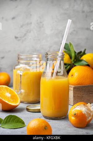 orange juice in glass bottles, fresh oranges and tangerines on a gray concrete background Stock Photo