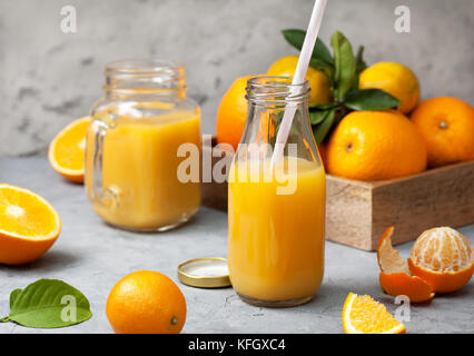 orange juice in glass bottles, fresh oranges and tangerines on a gray concrete background Stock Photo