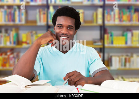 Portrait of smiling male university student studying at table in library Stock Photo