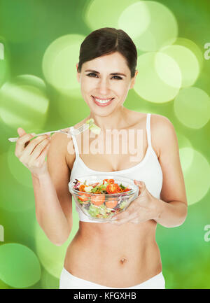 Portrait of healthy young woman eating salad against green background Stock Photo