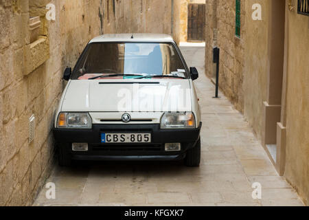 A Czechoslovakian Skoda car / vehicle parked too close to a wall in a narrow street / alley / road in the ancient walled city of Mdina in Malta. (91) Stock Photo