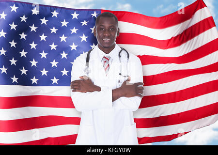 Portrait Of Confident Mature Male Doctor Standing In Front Of American Flag Stock Photo