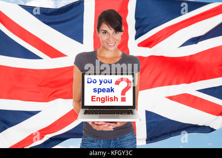Young Woman Holding Laptop Asking Do You Speak English In Front Of British Flag Stock Photo
